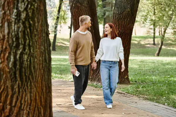 A couple, dressed casually, walk hand in hand in a park. — Stock Photo