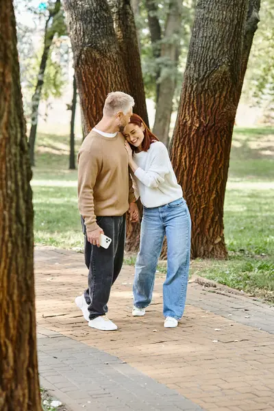 A man and woman in casual attire stand together in a park, surrounded by nature. — Photo de stock