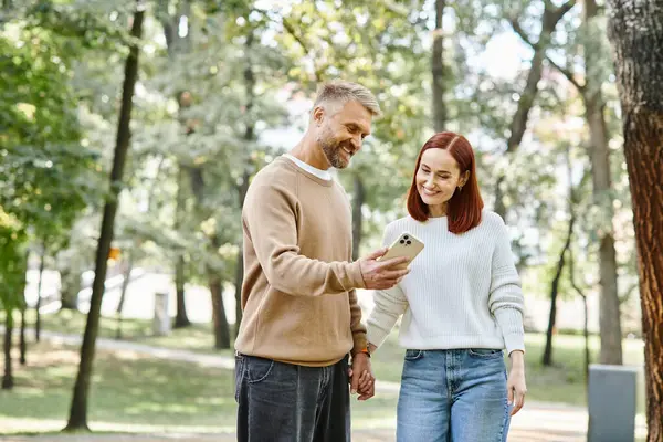 Couple standing in park, engrossed in cell phone. — Stock Photo