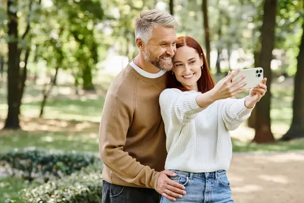 A man and woman in casual attire taking a selfie in a park. — Stock Photo