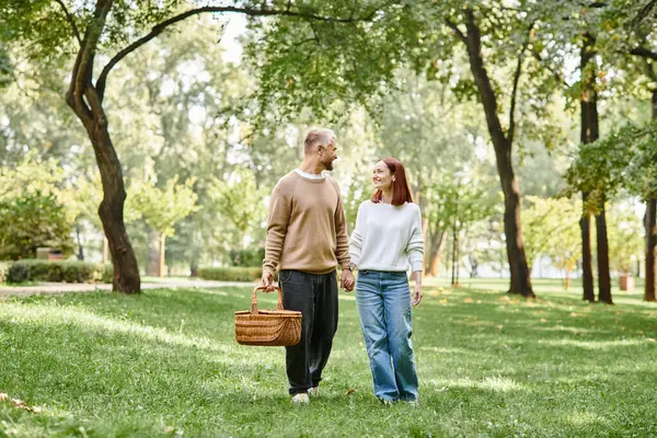 Un homme et une femme en tenue décontractée marchent main dans la main dans un parc paisible. — Photo de stock