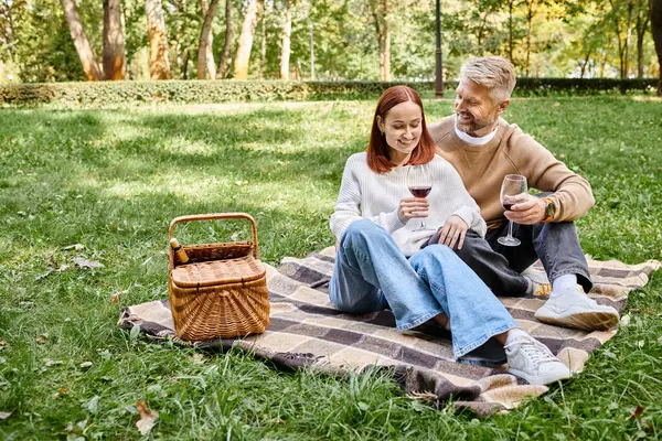 Um homem e uma mulher sentam-se em um cobertor na grama, desfrutando de um dia tranquilo no parque. — Fotografia de Stock