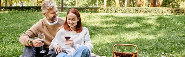 Взрослые мужчина и женщина сидят на одеяле, держа бокалы с вином в парке. — стоковое фото