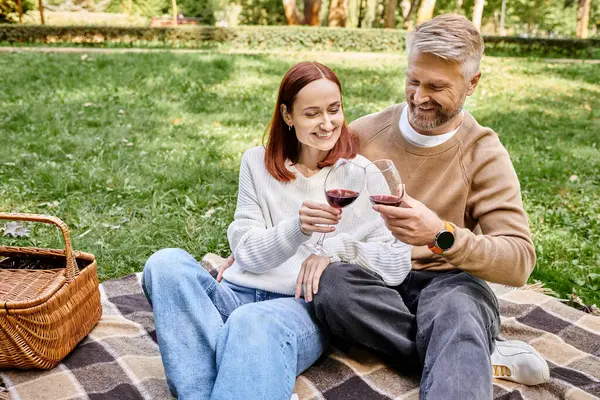 Um homem e uma mulher sentam-se em um cobertor acolhedor, segurando copos de vinho em um ambiente romântico. — Fotografia de Stock