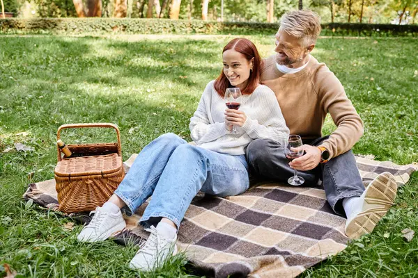 A man and woman in casual attire sitting on a blanket in the grass. — Stock Photo