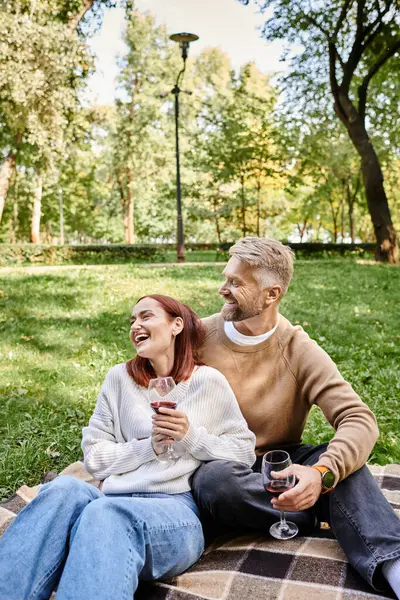 Una pareja en atuendo casual se sienta en una manta en un parque, disfrutando de un momento de paz juntos. - foto de stock