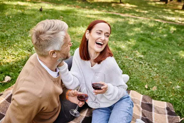 Um homem e uma mulher desfrutando de um piquenique romântico enquanto segurando copos de vinho. — Fotografia de Stock
