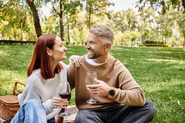 A couple sits on a blanket in a park holding wine glasses. — Stock Photo