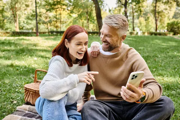 A couple enjoying a park picnic while looking at a cell phone. — Stock Photo