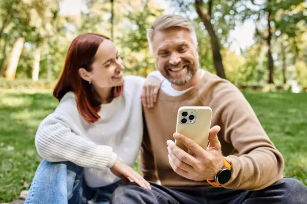 Una pareja disfrutando de la compañía de los demás mientras mira un teléfono celular en la hierba. - foto de stock