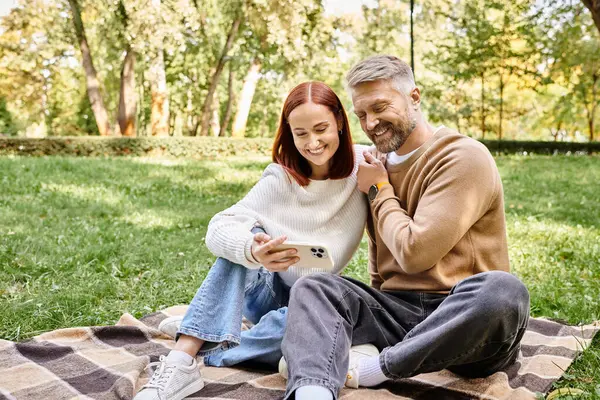 A man and a woman sit together on a blanket in a park, enjoying each others company. — Stock Photo