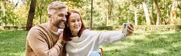 A man and woman in casual attire taking a selfie together in a park. — Stock Photo