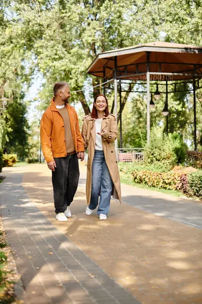 Un hombre y una mujer en atuendo casual caminan de la mano por un camino pacífico. - foto de stock