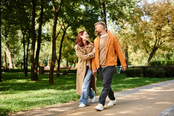 A man and woman in casual attire walk down a peaceful path in a lush park. — Stock Photo