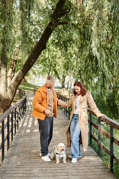 Couple adulte promener leur chien ensemble sur un pont dans un parc. — Photo de stock