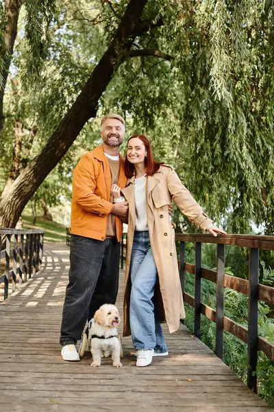 Adult couple in casual attire standing on a bridge with their beloved dog. — Stock Photo