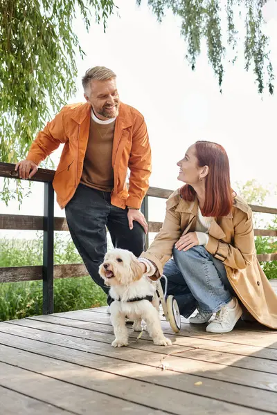 Loving couple in casual attire sit on a wooden deck, enjoying the outdoors with their dog. — Photo de stock
