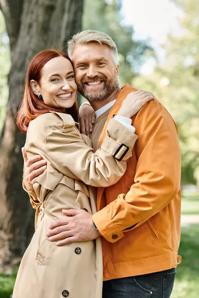 A man and a woman lovingly hug in a park while taking a leisurely walk. — Stock Photo