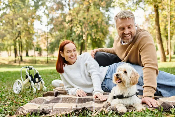A couple relaxes on a blanket in the park with their dog by their side. — Stock Photo
