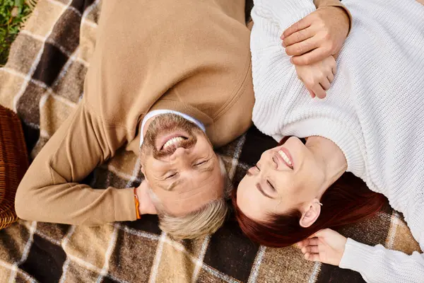 A man and a woman laying on a blanket in a serene park setting. — Stock Photo