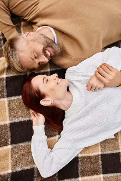 A man and a woman lay on a plaid blanket in a park, sharing a peaceful moment together. — Stock Photo