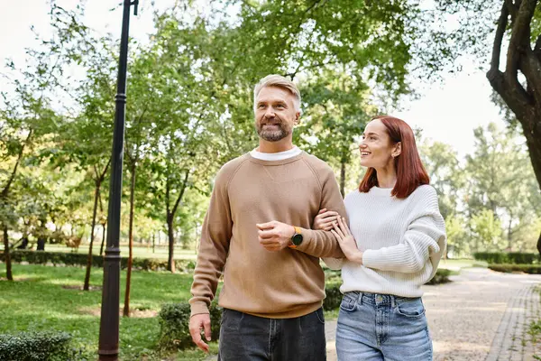 Couple aimant adulte en tenue décontractée marchant ensemble dans un cadre paisible du parc. — Photo de stock