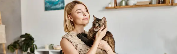 Una donna con i capelli corti culla teneramente il suo gatto tra le braccia a casa, condividendo un momento tranquillo di connessione. — Foto stock