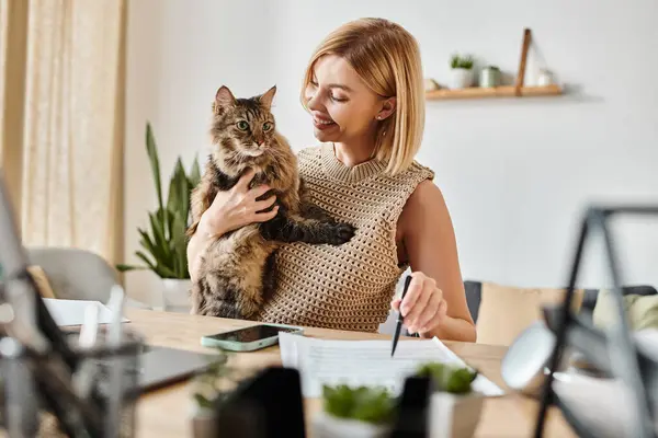 Une femme aux cheveux courts s'assoit à un bureau, tenant doucement son chat dans ses bras alors qu'ils partagent un moment paisible ensemble. — Photo de stock