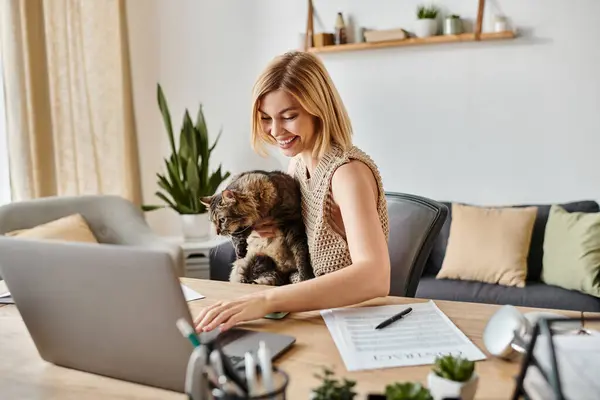 Una donna con i capelli corti siede tranquillamente a un tavolo con un gatto in grembo. — Foto stock