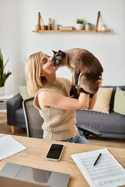 Une femme élégante avec des cheveux courts collant avec son chat bien-aimé en le tenant dans ses mains à la maison. — Photo de stock