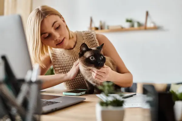 A woman with short hair holds a cat in front of a laptop, creating a cozy atmosphere at home. — Stock Photo