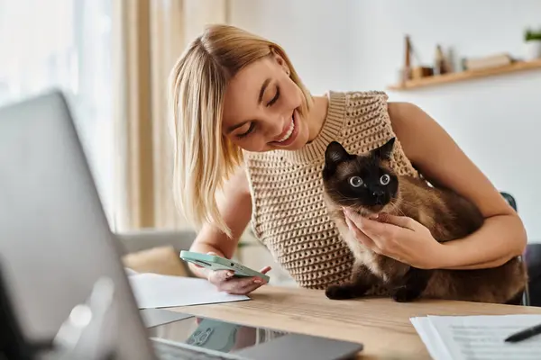 A woman with short hair sitting at a desk, lovingly holding a cat in her arms. — Stock Photo