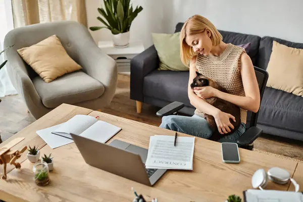 Una donna elegante con i capelli corti seduta su un accogliente divano, amorevolmente culla un gatto soffice tra le braccia. — Foto stock