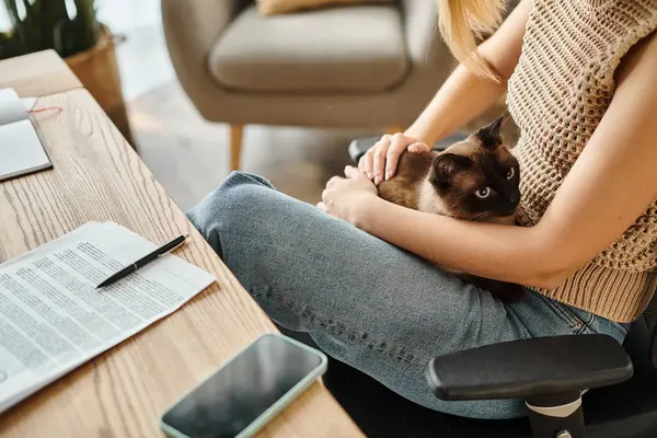 Una donna elegante con i capelli corti seduta su una sedia, tenendo delicatamente il suo gatto in modo amorevole a casa. — Foto stock