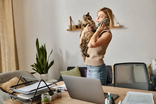 Una mujer con el pelo corto acaricia a su gato delante de un portátil, disfrutando de un momento acogedor en casa. - foto de stock