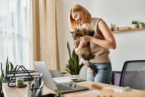 Una donna elegante con i capelli corti che tiene il suo gatto davanti a uno schermo del computer portatile, assorto in interazione digitale. — Foto stock