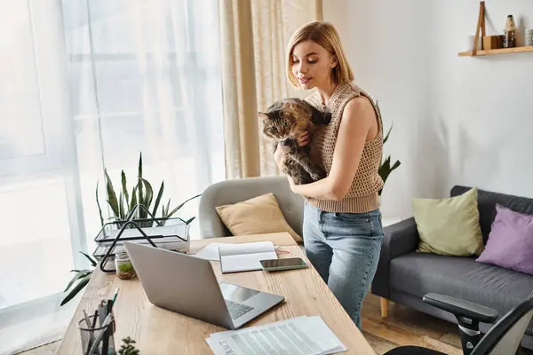 A woman with short hair standing in front of a laptop, holding her cat in a cozy moment at home. — Stock Photo