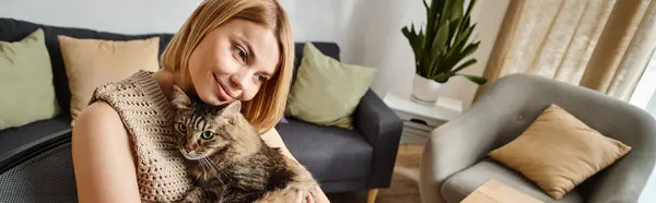 A content woman with short hair sits on a couch, lovingly holding her cat in a peaceful moment at home. — Stock Photo