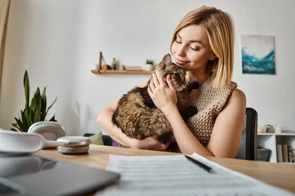 A stylish woman with short hair seated at a desk, gently holding and interacting with her furry cat companion. — Stock Photo