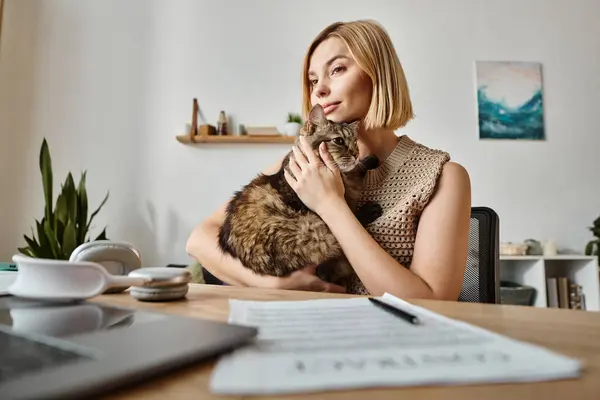 An attractive woman with short hair sits at a desk, holding and petting her content cat in a cozy indoor setting. — Stock Photo