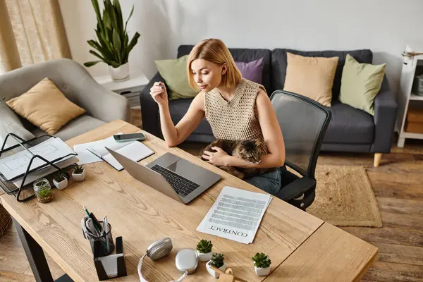 Uma mulher elegante com cabelo curto sentado em uma mesa com um laptop, acompanhado por seu gato em um ambiente acolhedor casa. — Fotografia de Stock