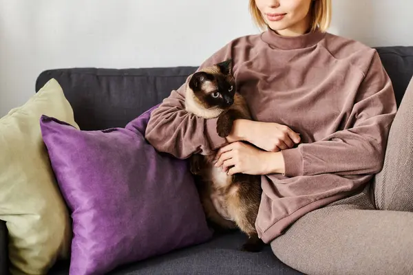 Serene woman with short hair sitting on a couch, lovingly holding her cat in a cozy home setting. — Stock Photo