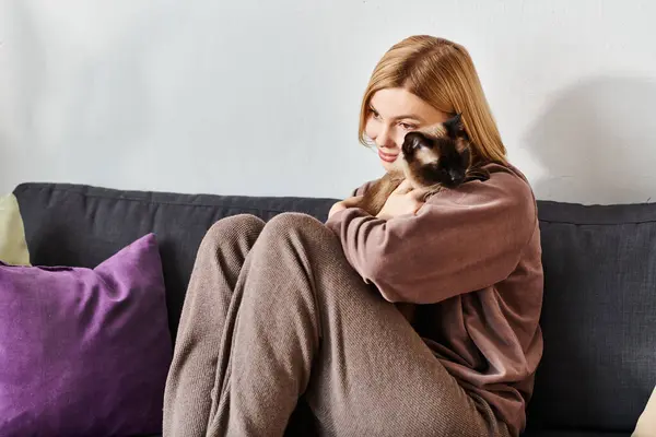 Una donna con i capelli corti si rilassa su un divano, cullando il suo gatto tra le braccia mentre condividono un momento di tranquillità insieme. — Foto stock