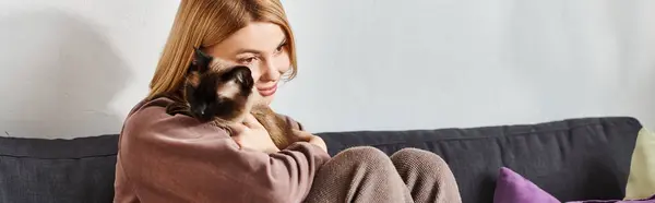 Una donna con i capelli corti coccola serenamente il suo gatto seduto su un divano. — Foto stock