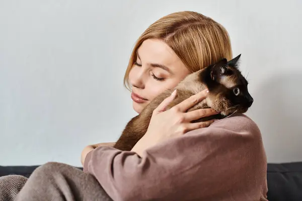 Una donna seduta su un divano con i capelli corti, teneramente tenendo il suo gatto in un ambiente domestico sereno e accogliente. — Foto stock