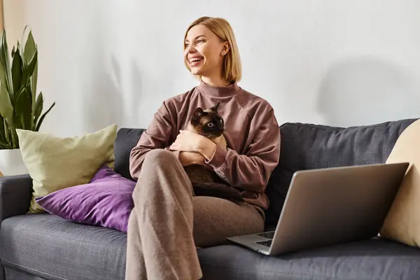 Жінка з коротким волоссям, сидячи на дивані, кидаючи кішку на руки, як виглядає задоволення і мирний. — стокове фото