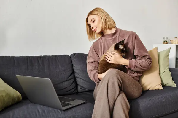 Una donna in un ambiente accogliente su un divano, stringendo il suo gatto vicino, incarnando un momento sereno di compagnia e relax. — Foto stock