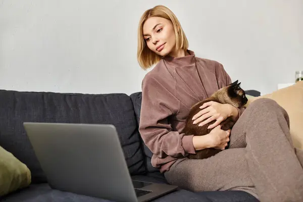 Una mujer con el pelo corto sentada en un sofá, sosteniendo tiernamente a su gato, compartiendo un momento de compañía tranquila en casa. - foto de stock