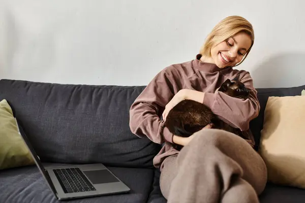 Una donna dai capelli corti si rilassa su un divano, cullando il suo gatto tra le braccia. Condividono un tranquillo momento di intimità e comfort. — Foto stock