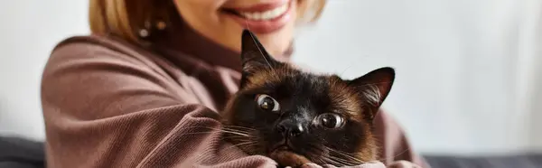 A stylish woman with short hair tenderly holds her cat in her arms, sharing a moment of love and companionship at home. — Stock Photo